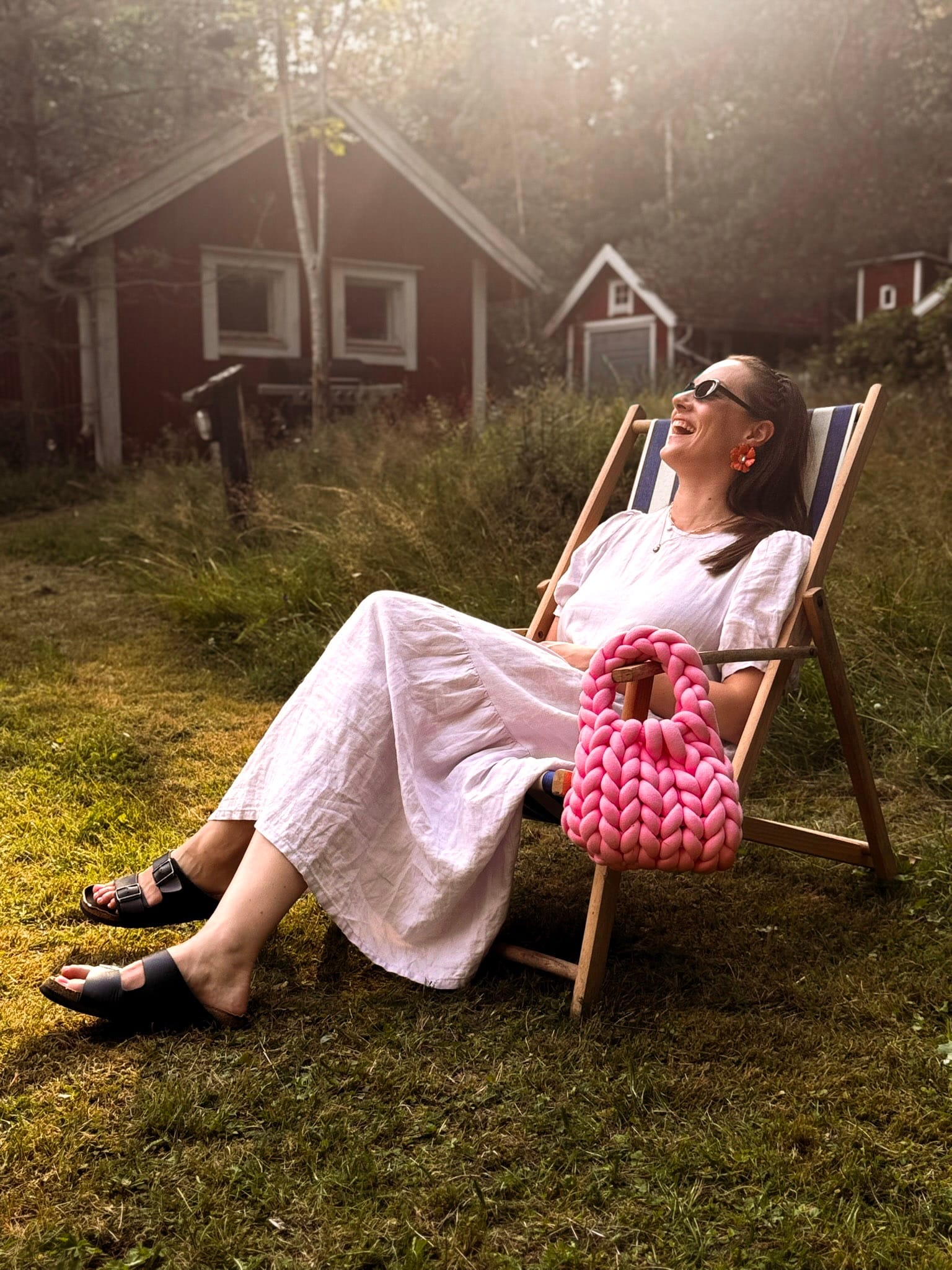 Laughing in a striped deckchair, a pink hand-crocheted MALLA bag resting on her lap.